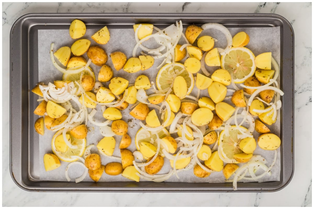 A large sheet pan lined with parchment paper with onions, potatoes and lemon slices on top.