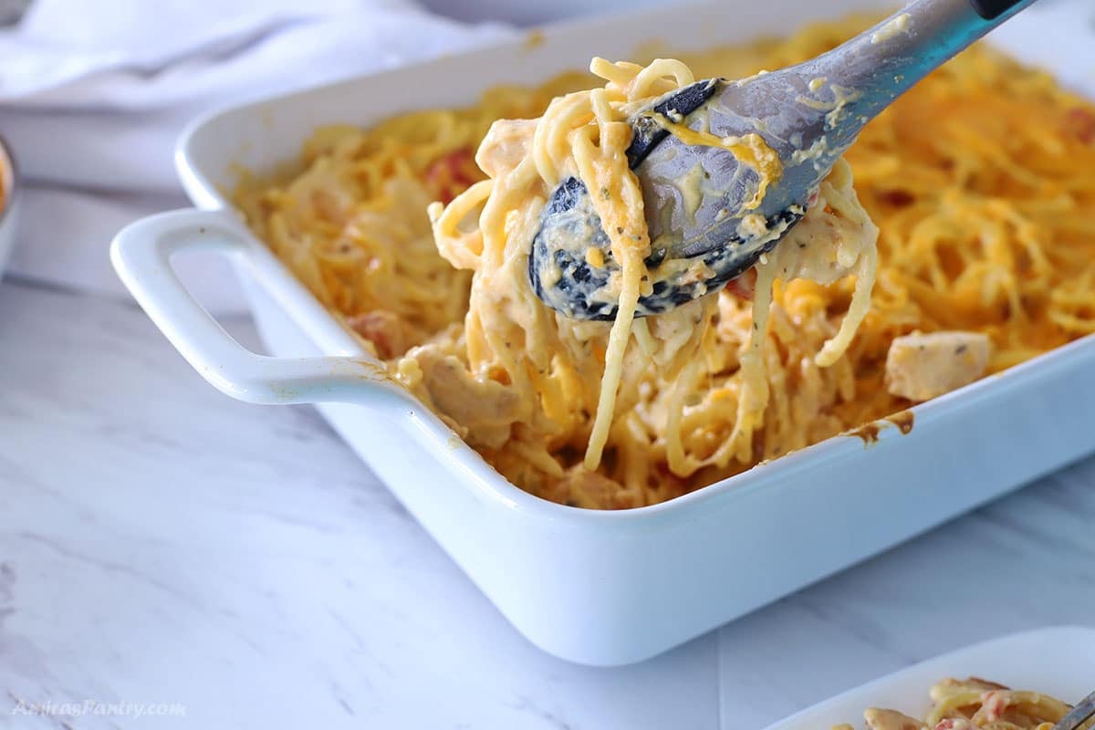 Kitchen tongs with spaghetti over a casserole dish.
