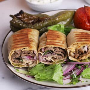 A close up image on a plate with Doner Kebab sandwiches on a bed of lettuce and Turkish sumac and onion salad.