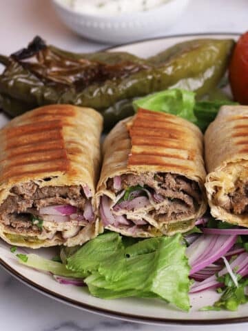 A close up image on a plate with Doner Kebab sandwiches on a bed of lettuce and Turkish sumac and onion salad.