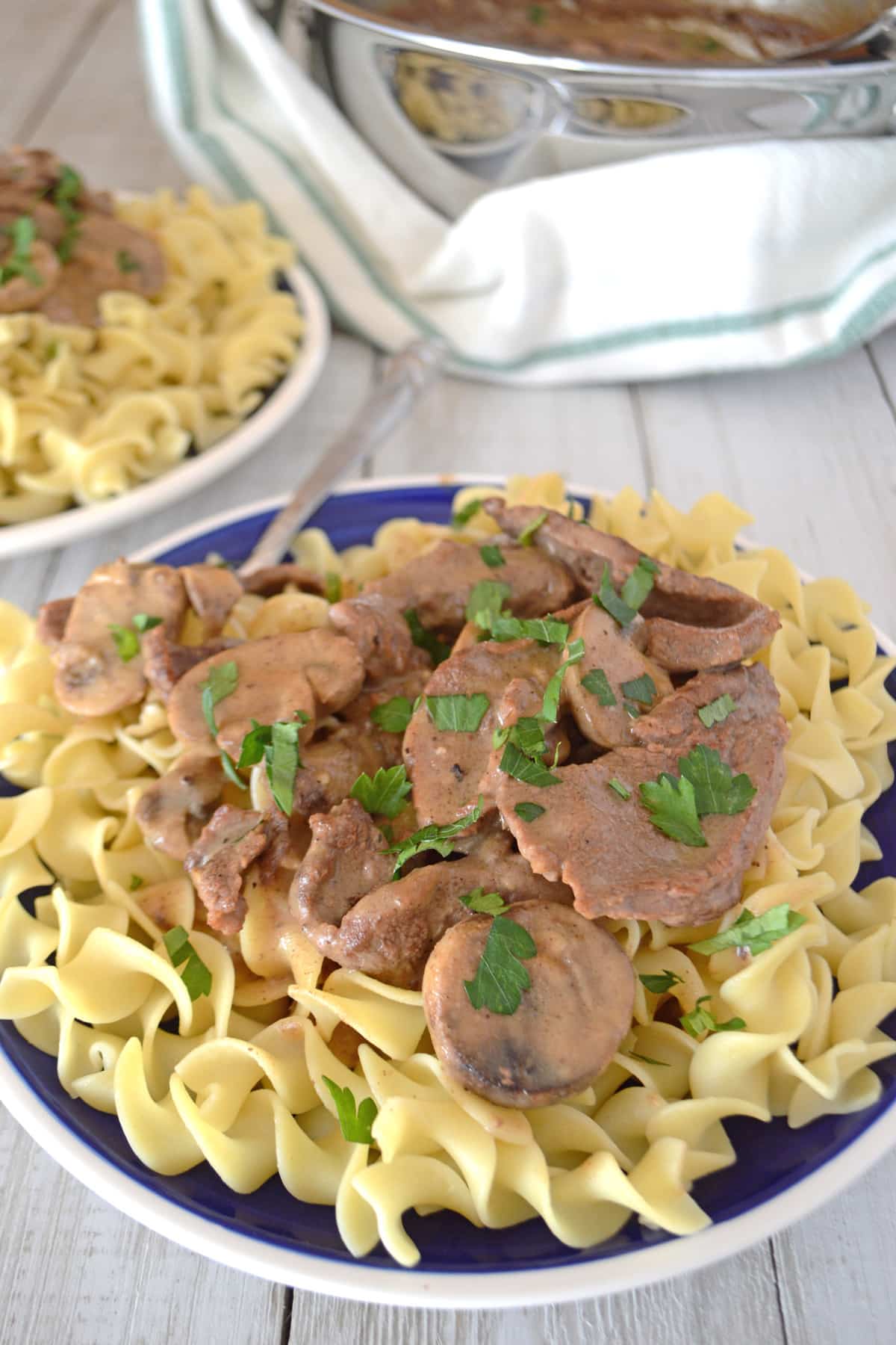 A blue plate filled with beef stroganoff on egg noodles.