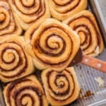 A spatula lifting one cinnamon roll out of the pan.