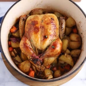 An over head image of a whole chicken over potatoes.