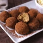 Tiramisu truffles on a white plate with a bite taken from one to show texture.