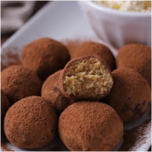 Tiramisu truffles on a white plate with a bite taken from one to show texture.