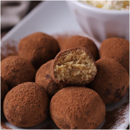 Tiramisu truffles on a white plate with a bite taken from one to show texture.
