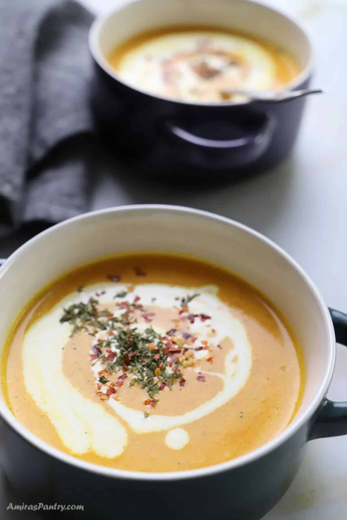Two bowls of lentil carrot soup garnished with crushed red pepper flakes and a drizzle of cream.