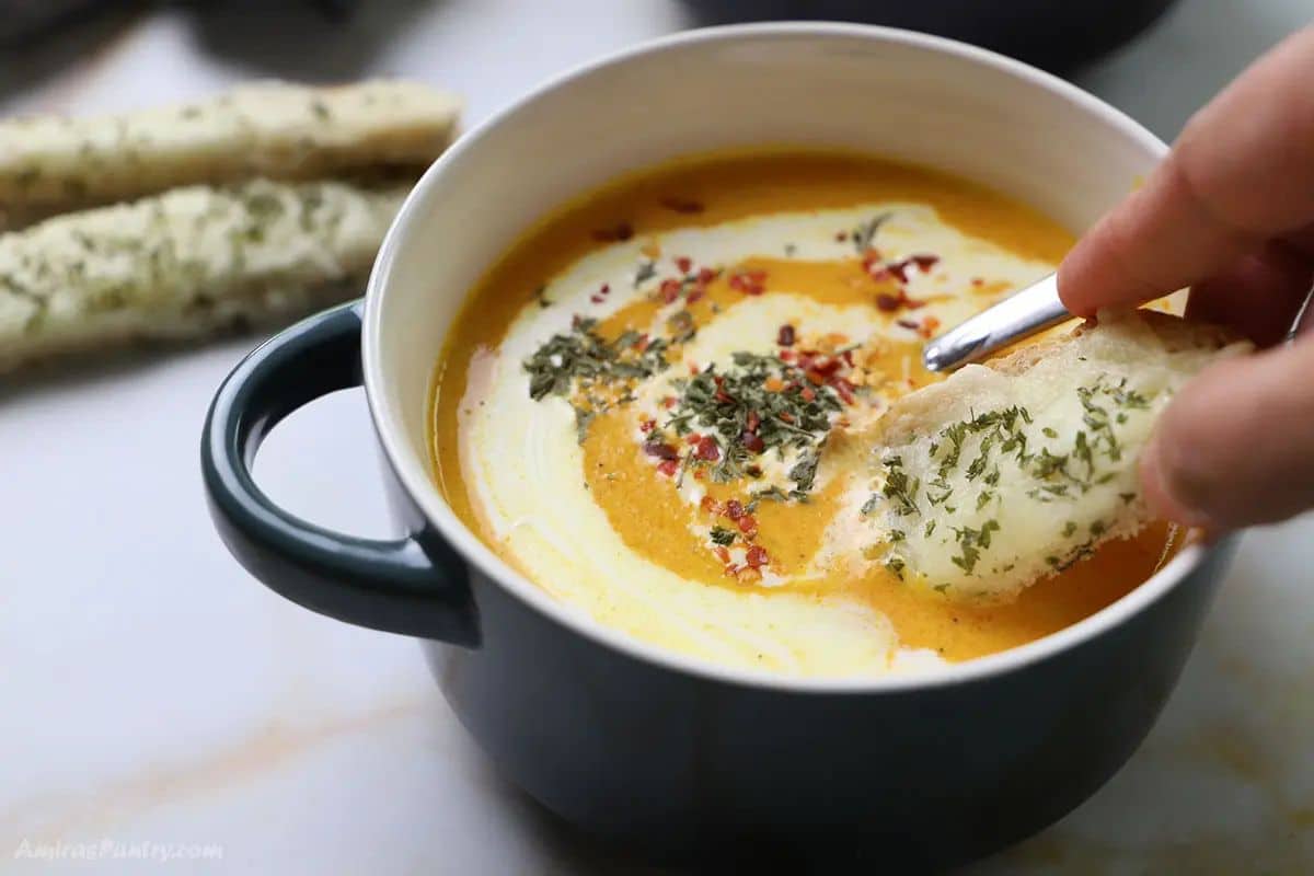 A hand dipping a piece of garlic bread into a bowl of soup.