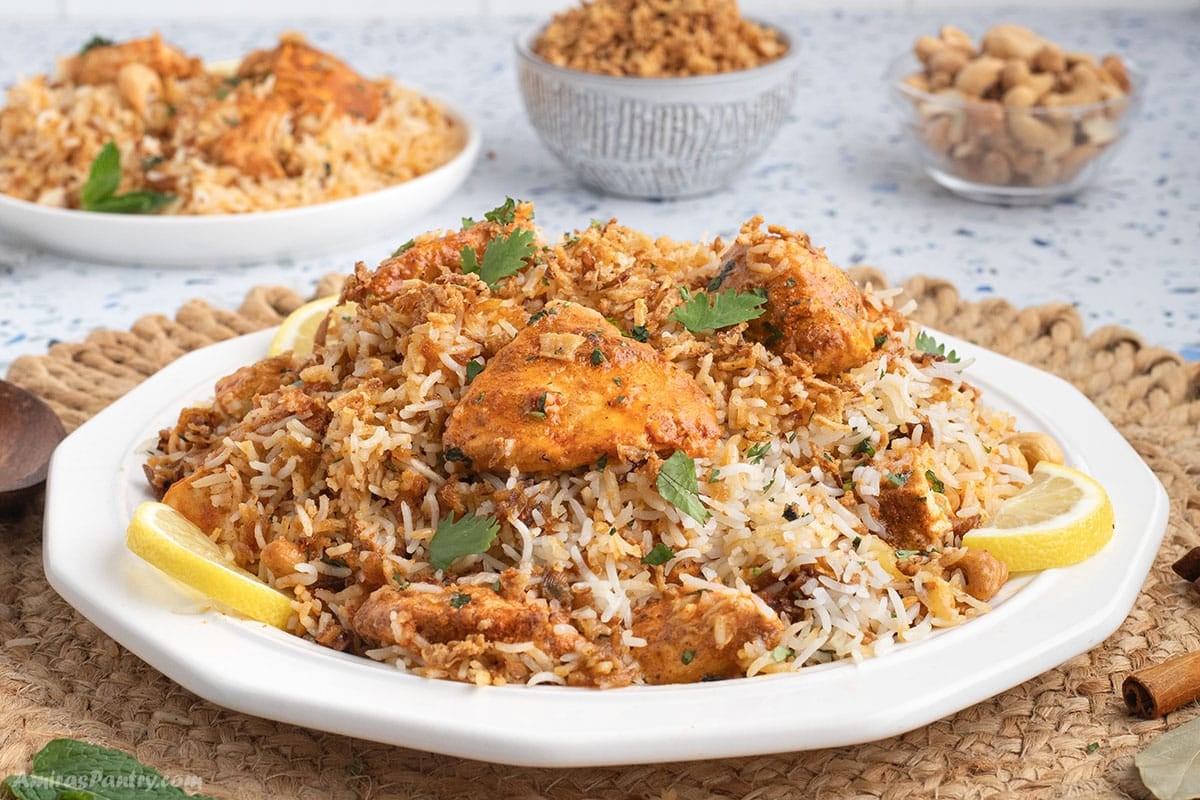 An image of a white dinner plate with chicken tikka biryani garnished with lemon slices.