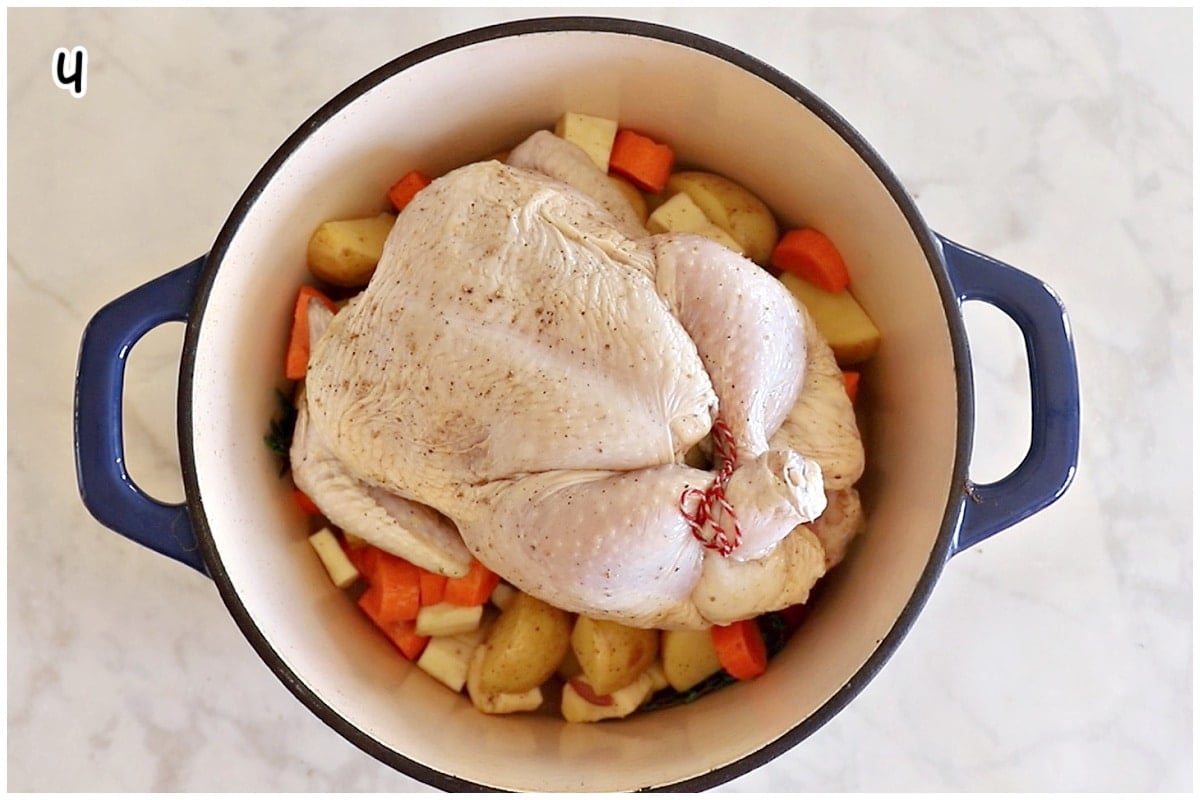 A dutch oven with vegetables topped with a whole chicken.