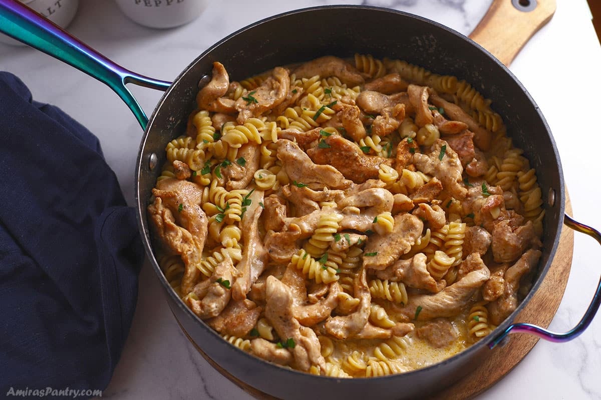 An overhead image of a large non stick skillet with cajun chicken pasta.