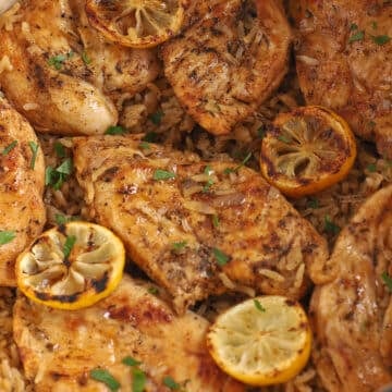 A close up image on cooked chicken breast on top of rice garnished with lemon.