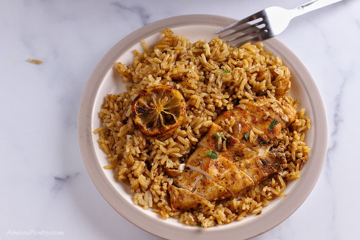 Sliced chicken breast over some herb rice with sliced lemon.