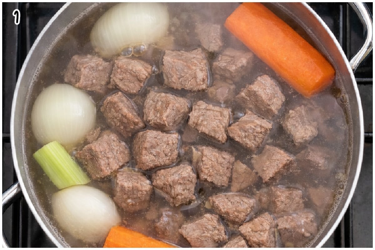 A large pot with beef cubes boiling in water with aromatics.