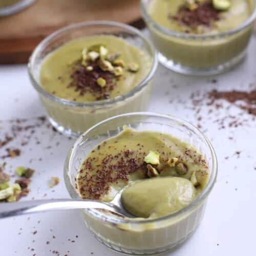 A spoon scooping some pistachio pudding off small glass ramekins.