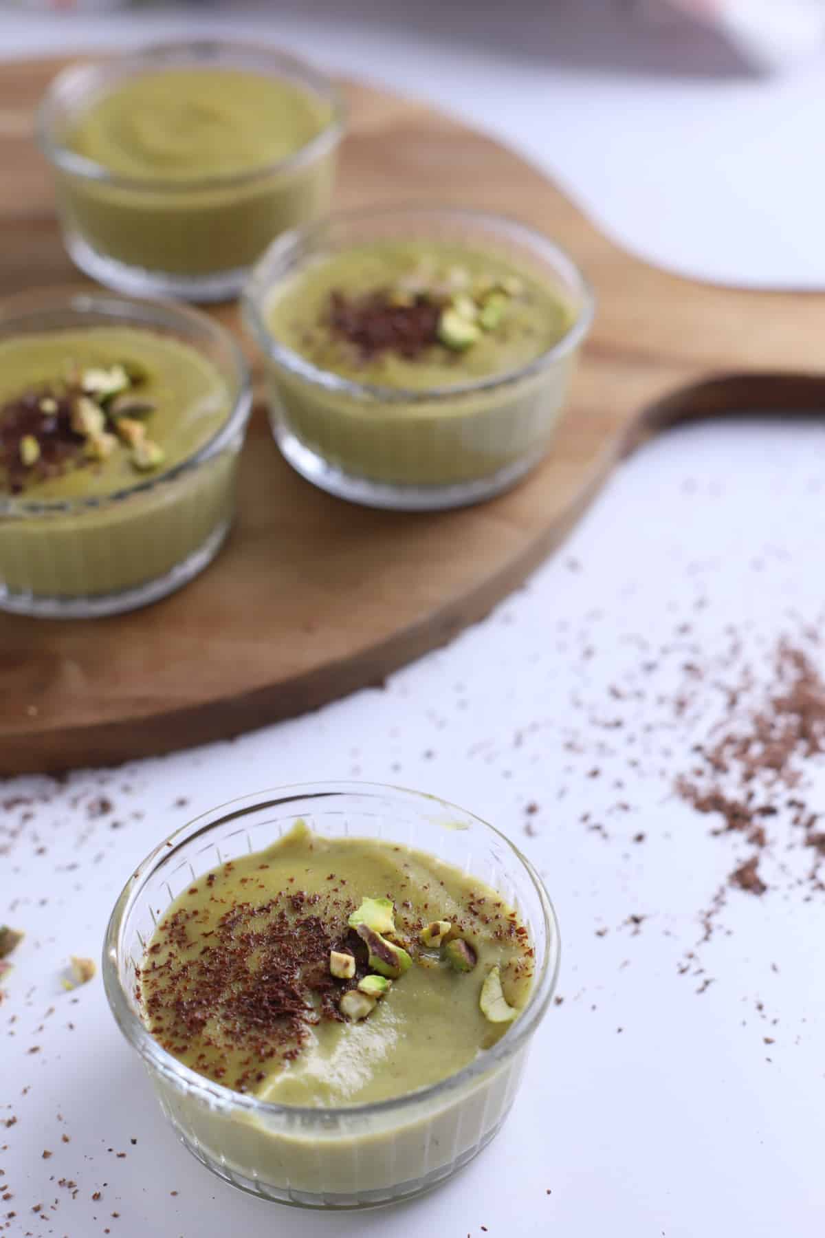 Pistachio pudding in glass ramekins garnished with shaved chocolate.