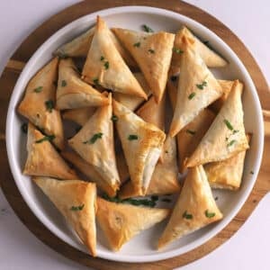 An overhead image of Spanakopita triangles on a white platter.