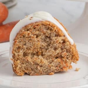 A slice of carrot bundt cake on a small serving plate with carrots in the back.