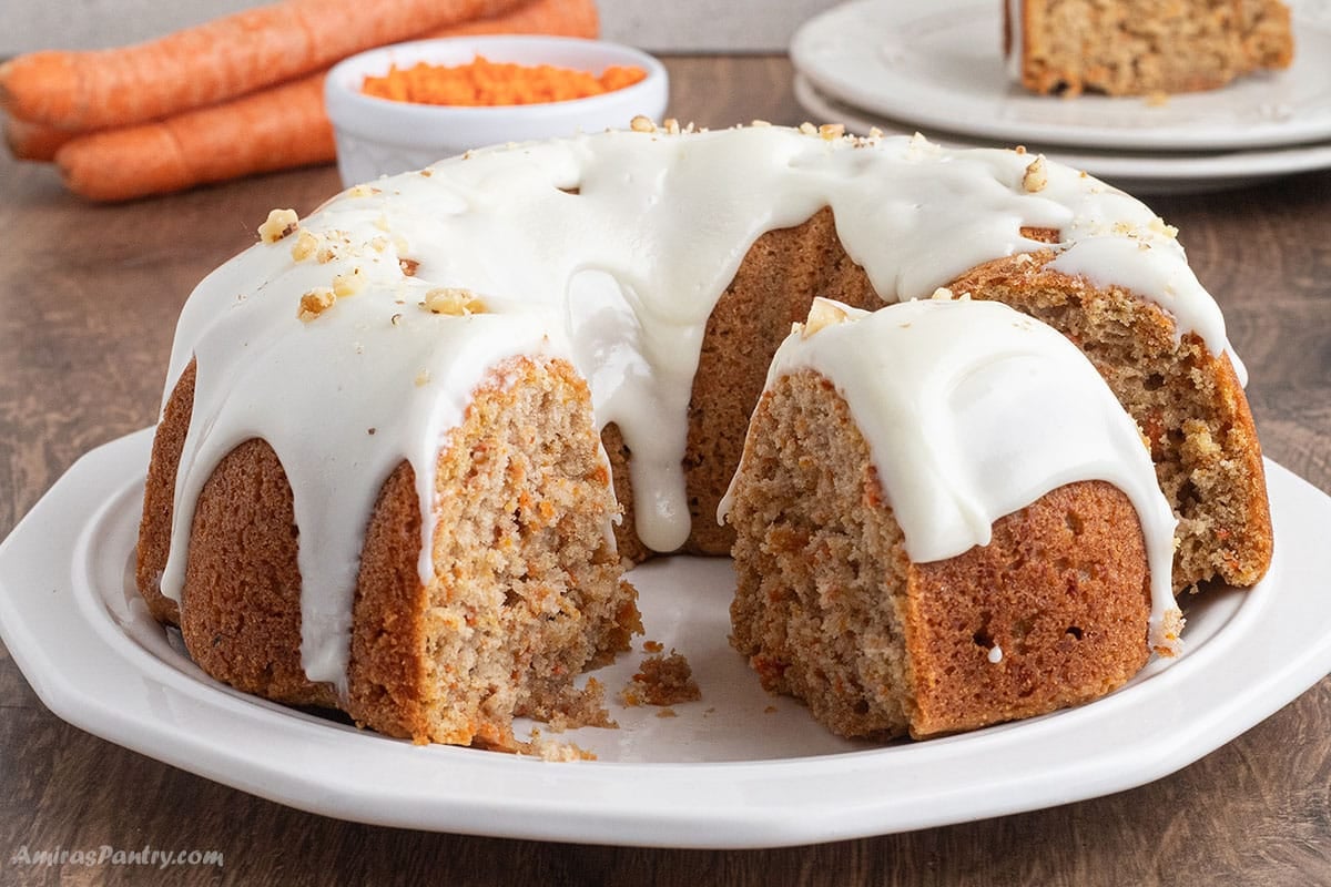 Carrot cake on a white platter sliced and glazed with cream cheese.