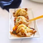 Three dumplings on a serving plate with chopsticks.