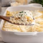 A wooden spatula scooping a serving of he lasagna rolls.