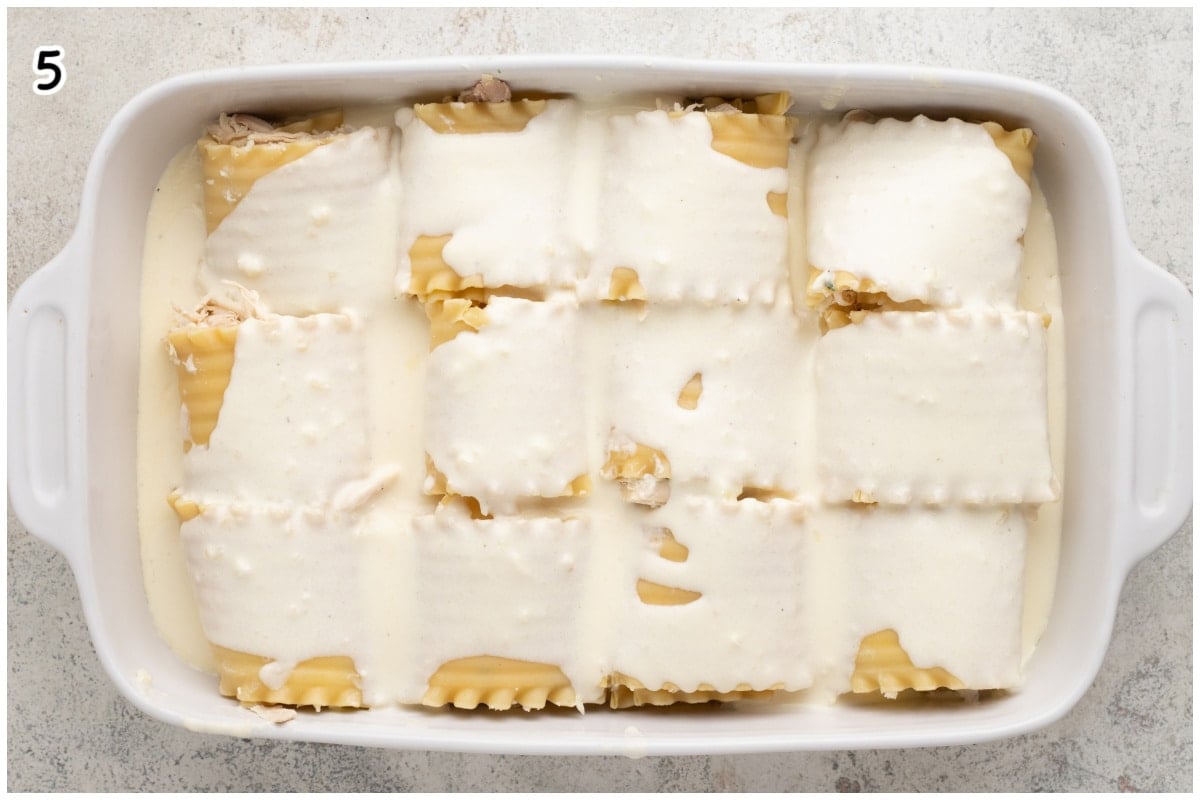 A white casserole dish with lasagna rolls topped with homemade alfredo sauce.