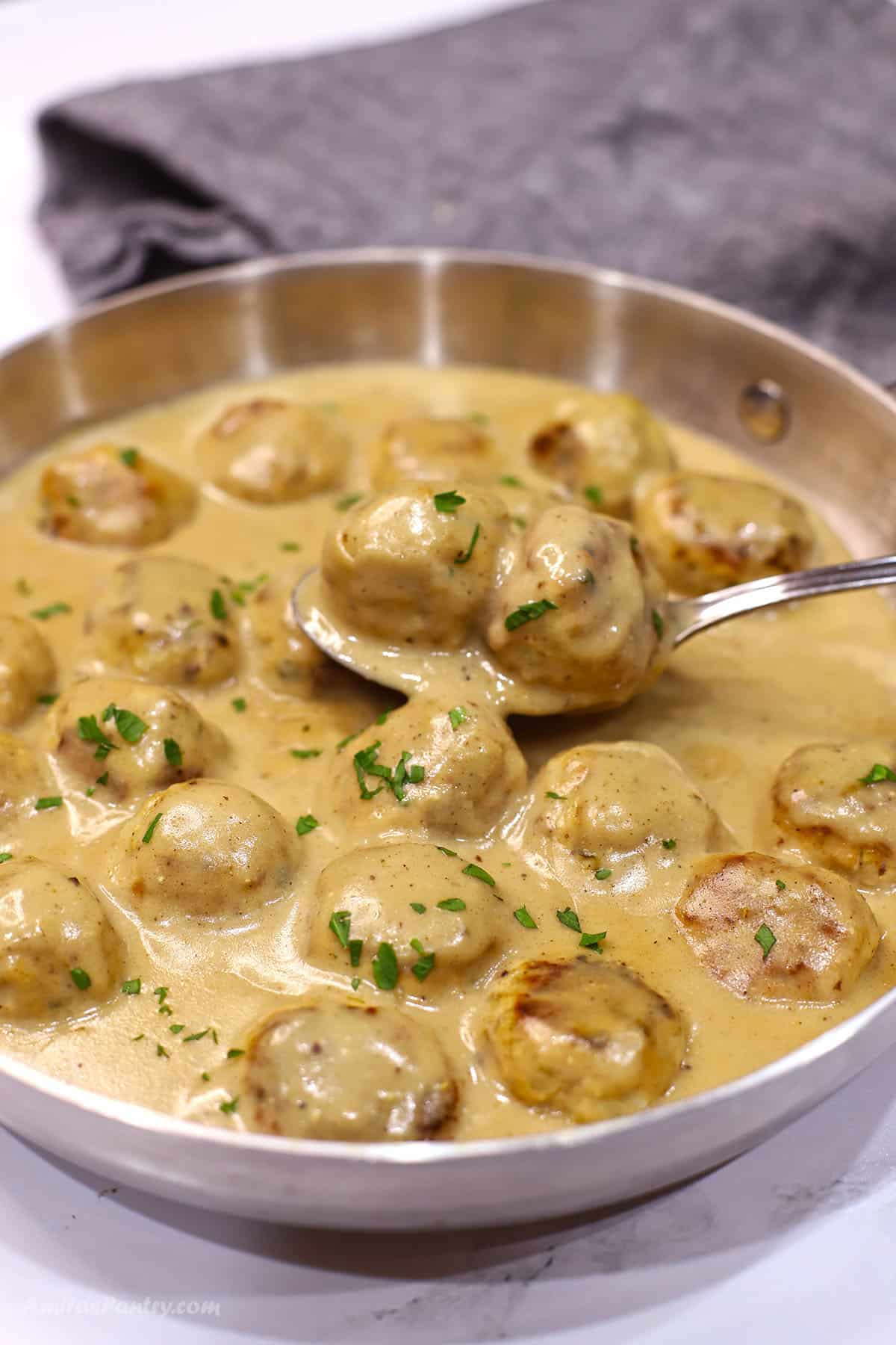 A large skillet with chicken Swedish meatballs in creamy sauce.