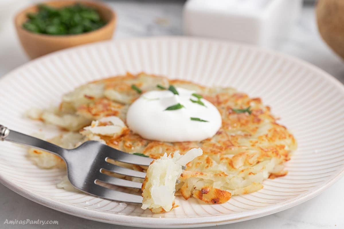 A potato rosti topped with sour cream on a white plate.