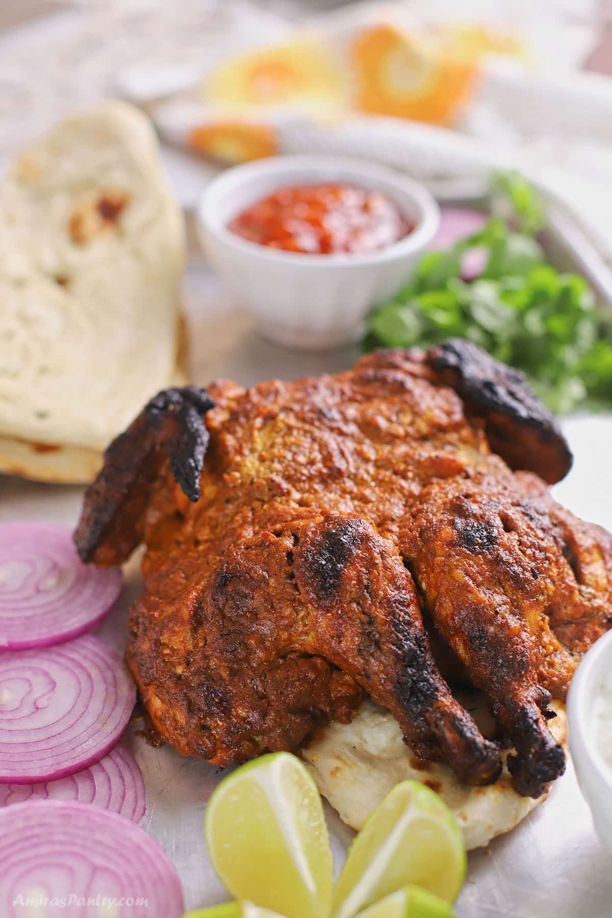 A tandoori whole chicken on a baking sheet with red onions and bread.
