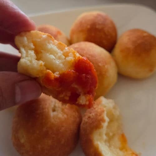 A hand holding a cheese ball dipped in red sauce.