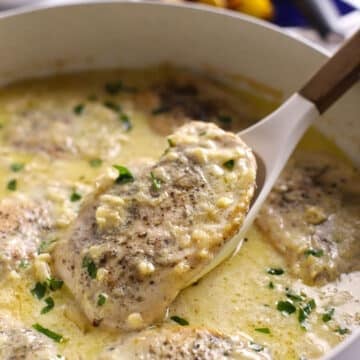 Close up of creamy Dijon chicken in a skillet, with a tender chicken breast lifted on a spoon and topped with fresh parsley.