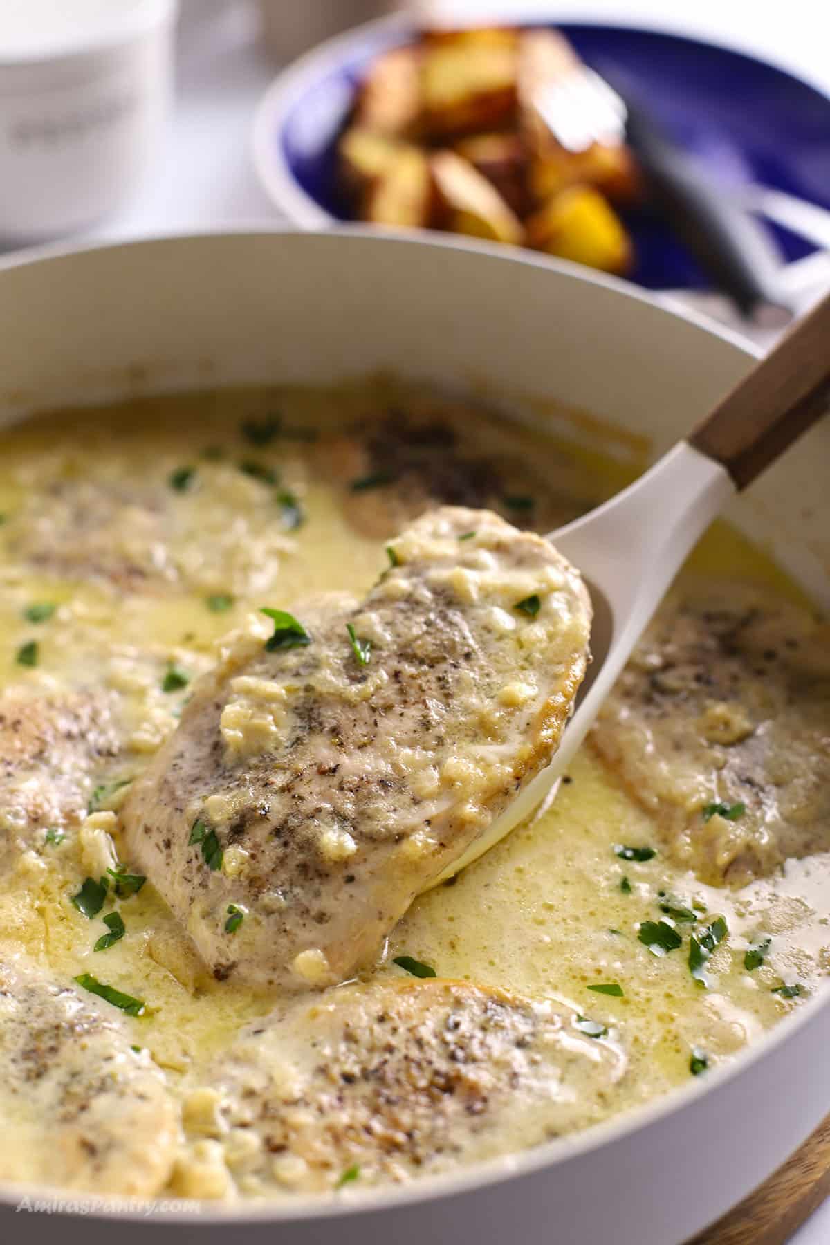 Close up of creamy Dijon chicken in a skillet, with a tender chicken breast lifted on a spoon and topped with fresh parsley.
