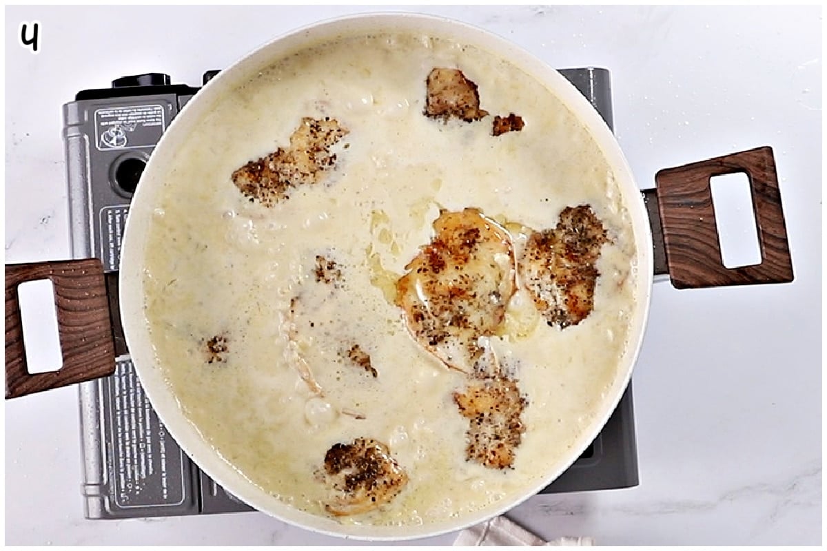Overhead view of seared chicken pieces simmering in a creamy Dijon sauce in a large skillet on the stovetop.