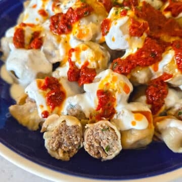 Manti dumplings on a serving plate drizzled with yogurt sauce.