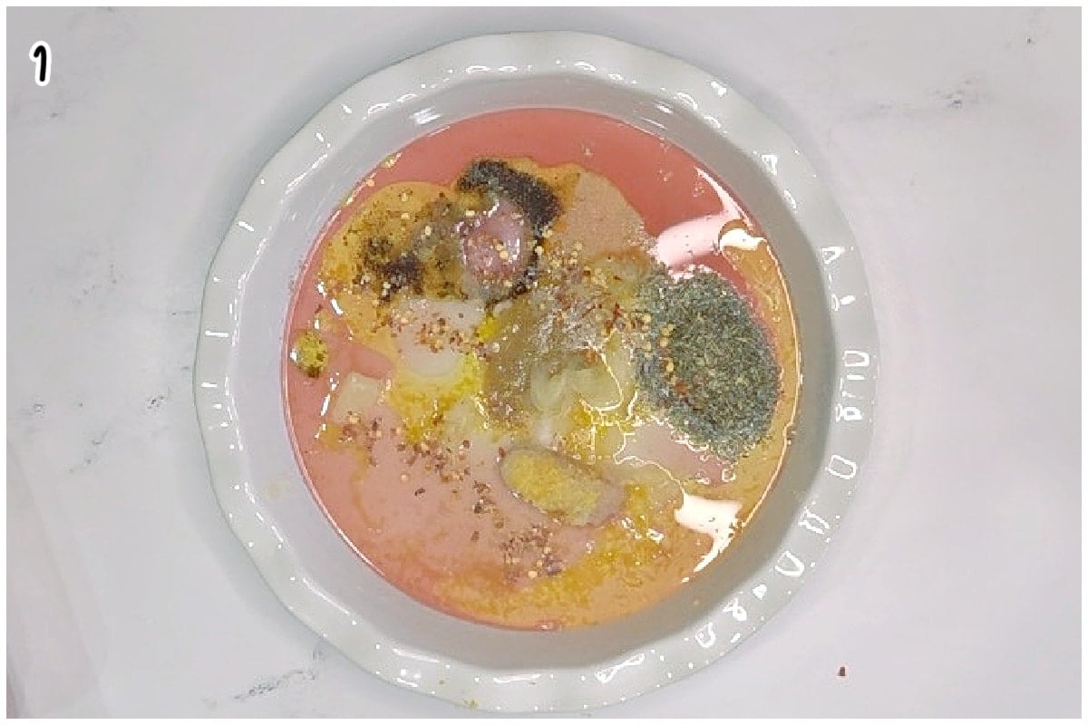 Overhead view of a bowl filled with Italian grilled chicken marinade ingredients, including oil, seasonings, garlic, and herbs before mixing.