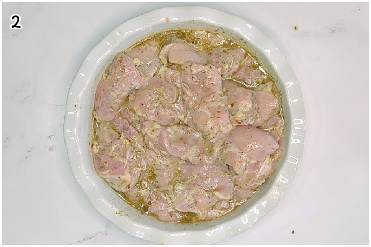 Overhead view of raw chicken pieces coated in a creamy Italian herb marinade in a white bowl, ready to marinate before grilling.