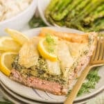Angled close-up of Salmon Wellington served on stacked plates, showing layers of flaky puff pastry, juicy baked salmon, and rich creamy spinach filling.