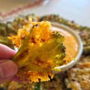 A hand holding a single, crispy piece of smashed broccoli showing its crisp edges and texture.