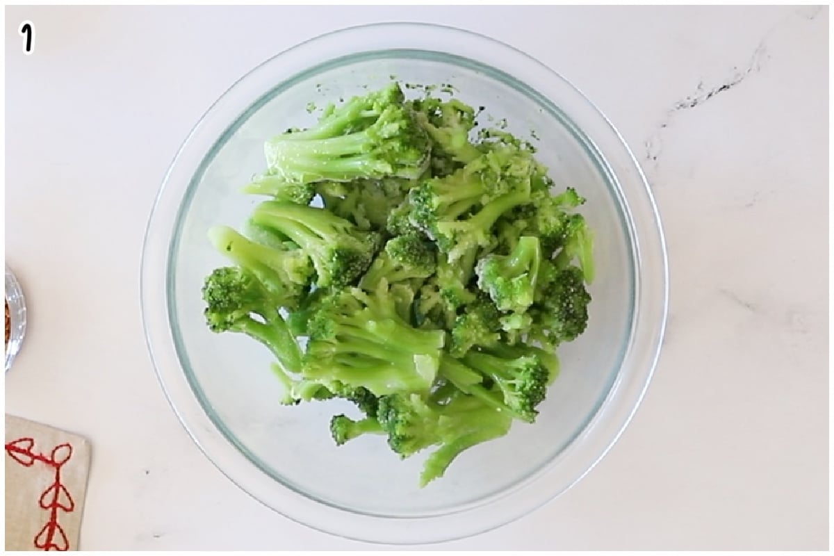 An overhead view of vibrant green, frozen broccoli florets in a clear glass mixing bowl.
