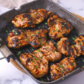 Balsamic chicken thighs on a grilling pan garnished with chopped parsley.