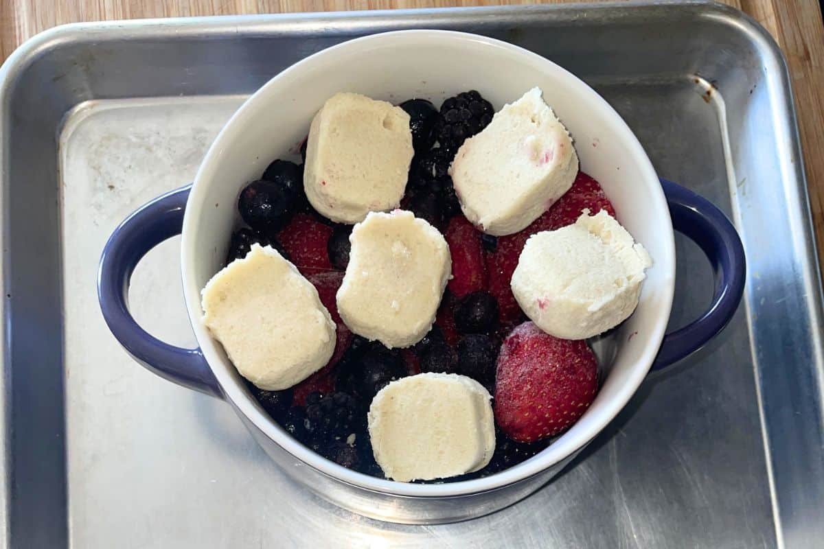 Overhead view of mixed berries topped with sliced refrigerated cookie dough in a small white baking dish, ready to go into the oven.