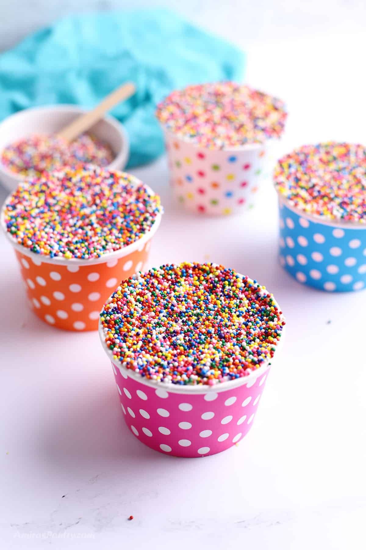 Polka dot paper cups filled with cake topped with frosting and rainbow sprinkles, served as individual dot cakes.