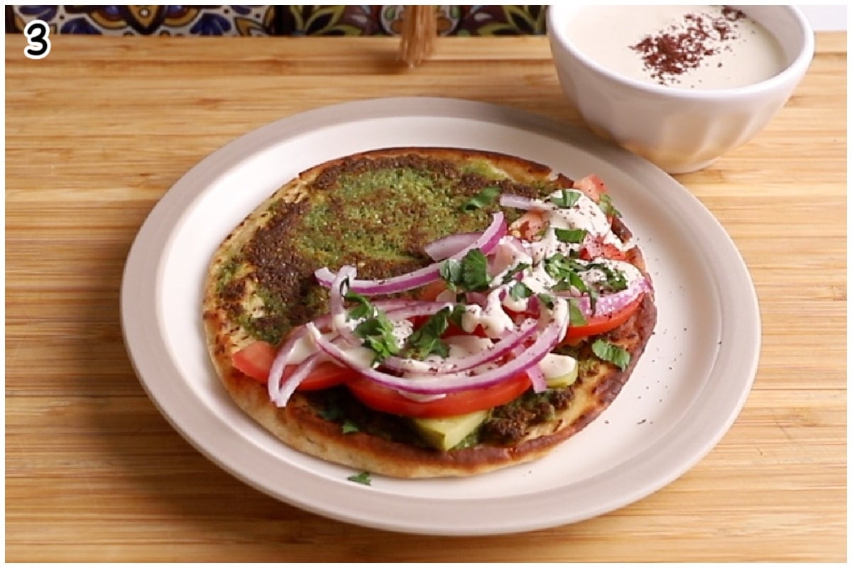 A finished falafel taco served open faced on a white plate on a wooden board loaded with falafel toppings.