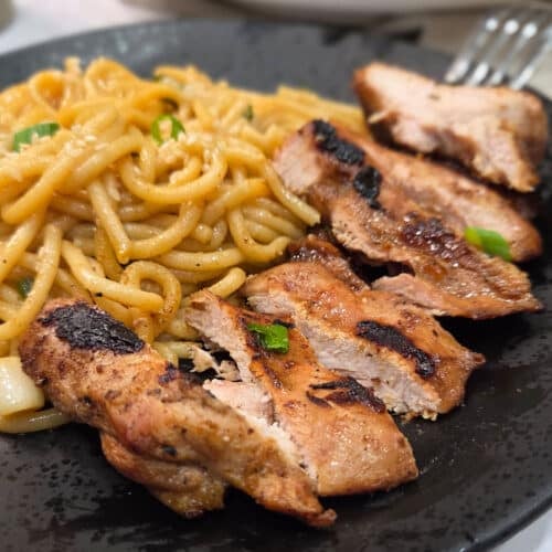 A close up image on a black plate with grilled chicken and noodles.