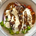 Close up overhead view of a crispy rice salad bowl with spiced ground meat, creamy white sauce, cucumbers, cherry tomatoes, and red onion.