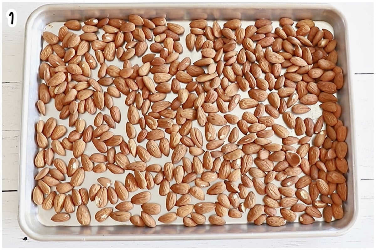 Raw almonds spread in a single layer on a baking sheet.