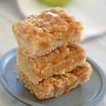 Three stacked apple crisp bars topped with oat crumble and caramel drizzle.