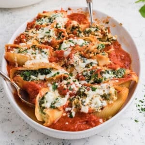 Baked conchiglioni pasta shells stuffed with spinach and ricotta cheese in a bed of red marinara sauce.
