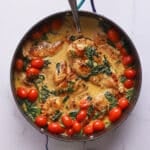 Overhead view of creamy Italian chicken with spinach and cherry tomatoes in a skillet with a spoon.