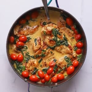 Overhead view of creamy Italian chicken with spinach and cherry tomatoes in a skillet with a spoon.